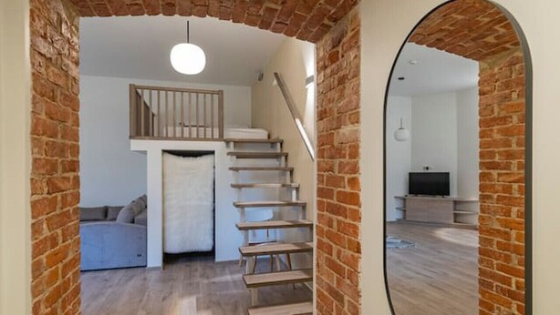 Un couloir avec une arche en briques, un escalier, un miroir et un luminaire.