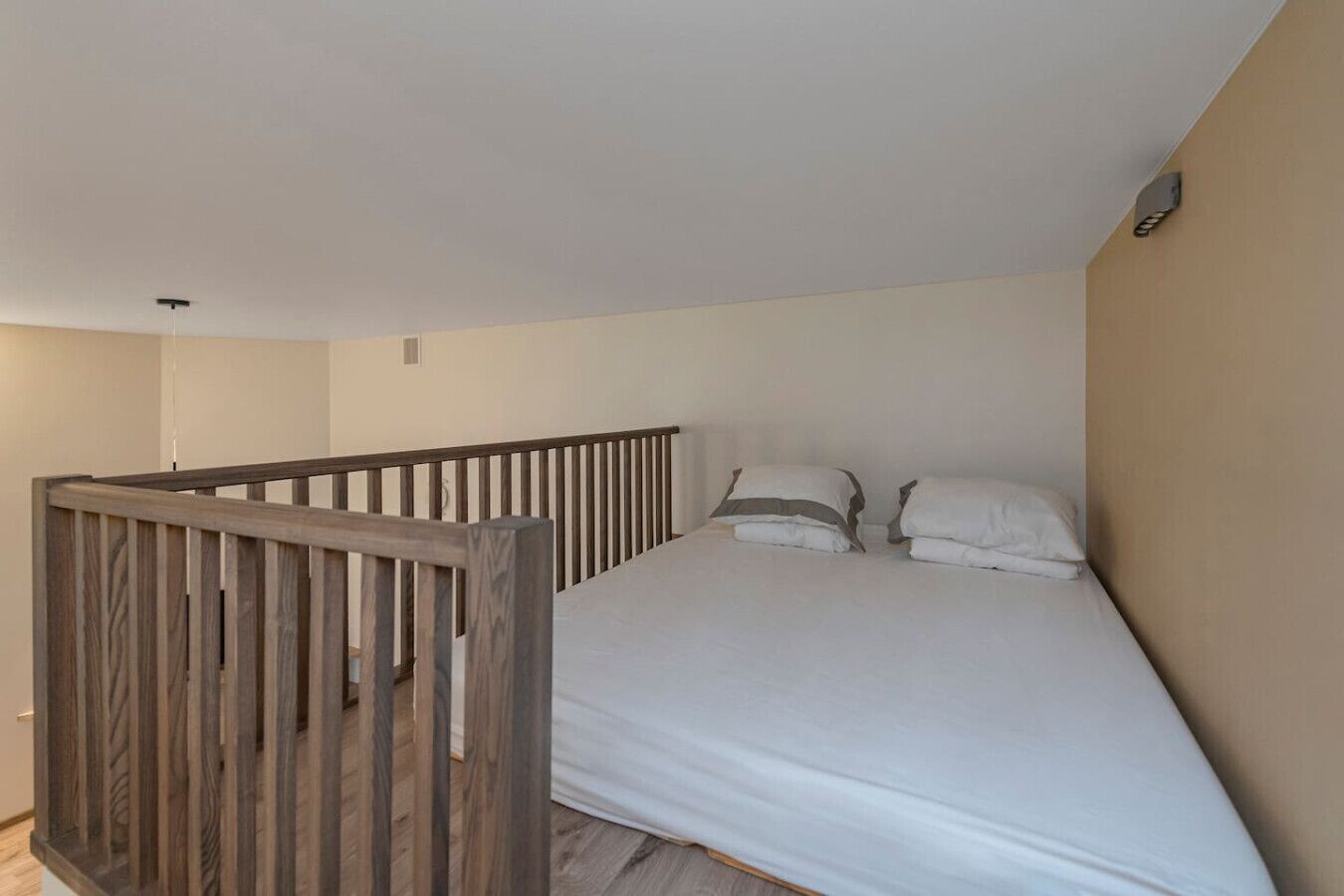 A bedroom with a wooden railing, a bed with white bedding, and a plain wall.