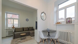 A living room with a sofa, a small round table, two chairs, a clock, and a window with a view.