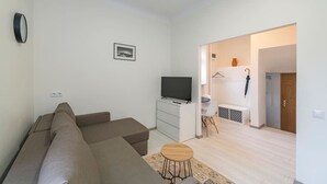 A modern living room with a sofa, a TV, a small table, and a hallway leading to a bathroom.