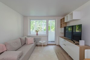 Un salon moderne avec un canapé, un téléviseur, une petite table et une fenêtre donnant sur un paysage verdoyant.