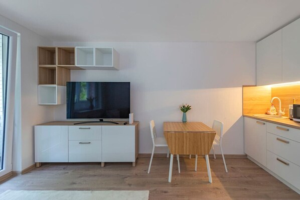 Une cuisine moderne équipée d’un téléviseur à écran plat, d’une table à manger avec des chaises et d’un petit îlot de cuisine doté d’un four à micro-ondes.