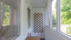 Un estrecho pasillo con un banco de madera y una pared de celosía, ventanas amplias a ambos lados y una planta en maceta a la izquierda.