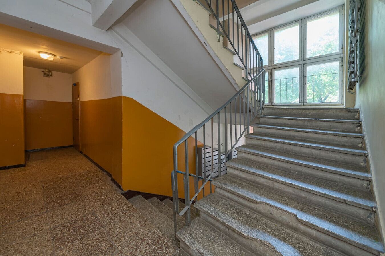Uma escadaria com corrimãos de metal, degraus carpetados e uma janela com vista para árvores.