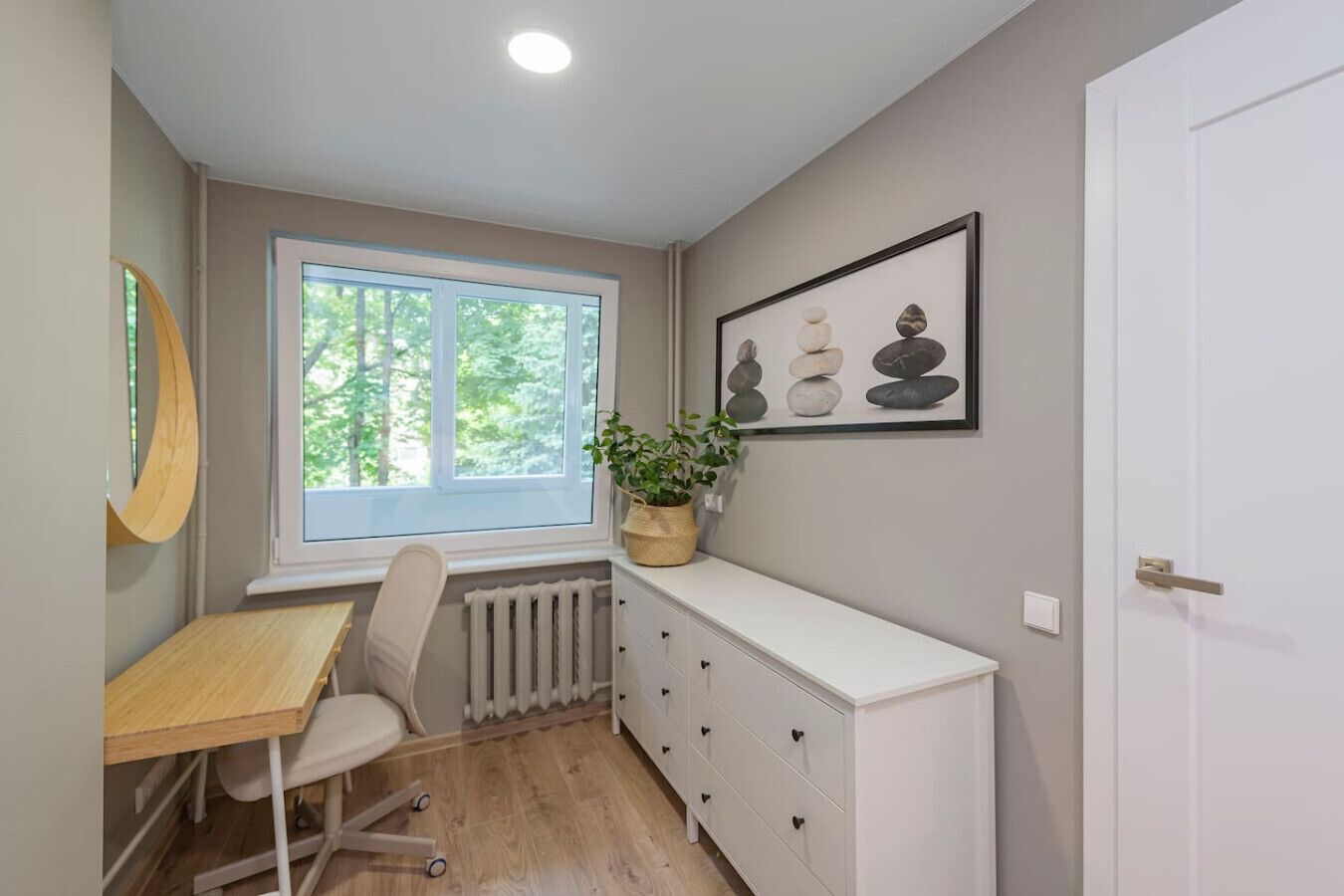 Una habitación con ventana, escritorio, silla, radiador, armario y puerta.
