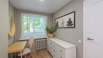 Una habitación con ventana, escritorio, silla, radiador, armario y puerta.