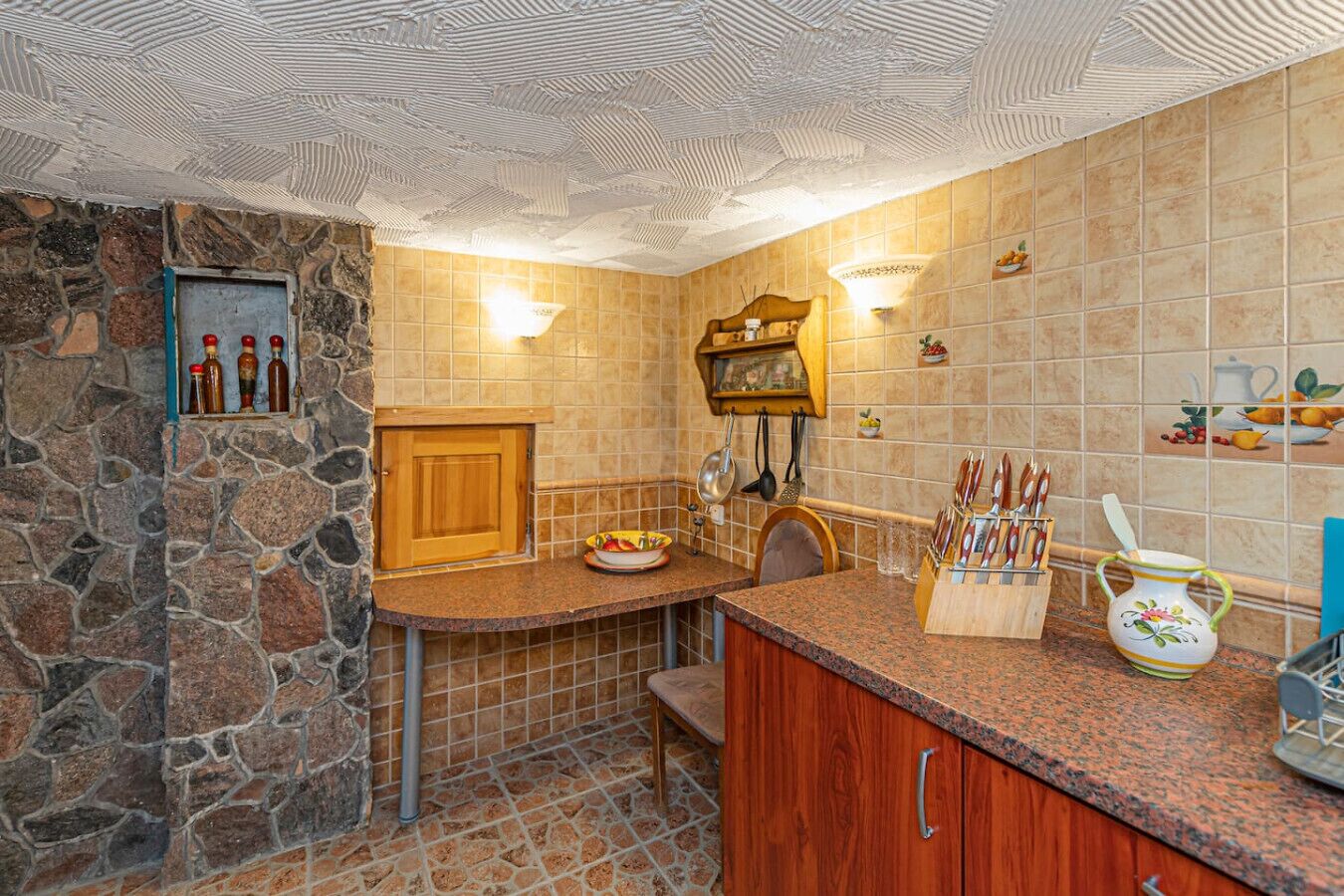 Une cuisine avec des murs en pierre, une porte en bois, un plan de travail en granit et divers ustensiles de cuisine.