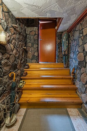 Un muro de piedra, escalones de madera, una puerta de madera y una pequeña estatua.