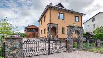 A two-story house with a stone entrance gate, a wooden staircase, and a brick pathway.