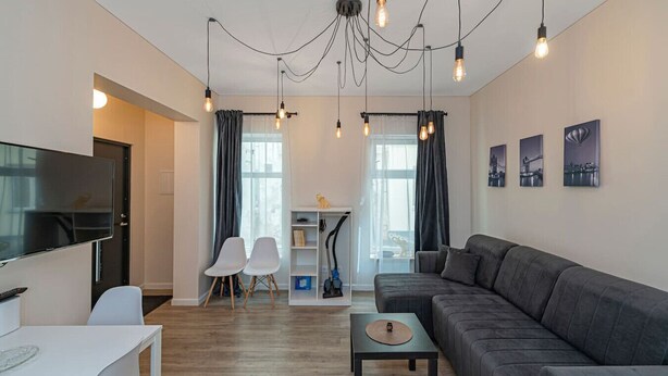 A modern living room with a sofa, a TV, a dining area, and a staircase. - Studio ap Contrast by Polo Apartments (Kaunas)