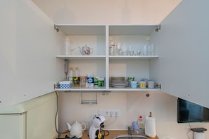 A kitchen with white cabinets, a kettle, a coffee machine, and various kitchen items on shelves.