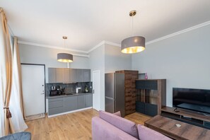 Ett modernt kök med grå skåp, ett kylskåp och en matplats med ett träbord och en lila soffa.