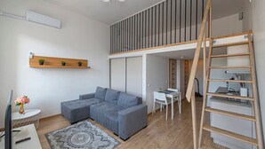 Een moderne woonkamer met een grijze modulaire bank, een kleine witte tafel, een ladder en een houten plank.