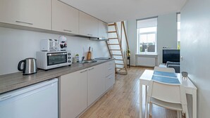 Een moderne keuken met een magnetron, broodrooster en waterkoker, een houten trap, een eethoek met een tafel en stoelen, en een televisie op de achtergrond.