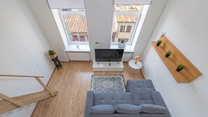 Een moderne woonkamer met een grijze bank, een televisie, een klein rond tafeltje en een houten plank met planten.