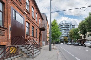 Une vue de rue avec un bâtiment en briques, une structure moderne en verre et des voitures garées.
