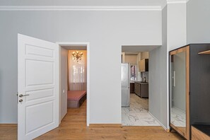 Un couloir avec une porte blanche, un banc et un coin cuisine équipé de placards et d’un réfrigérateur.