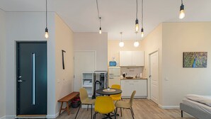 A compact living space with a kitchenette, a dining area with yellow chairs, a bed, and a door. - Downtown delight studio by Polo Apartments (Kaunas)