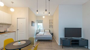 A compact hotel room with a bed, a TV, a dining area with chairs, a kitchen area, and a window with a view. - Downtown delight studio by Polo Apartments (Kaunas)