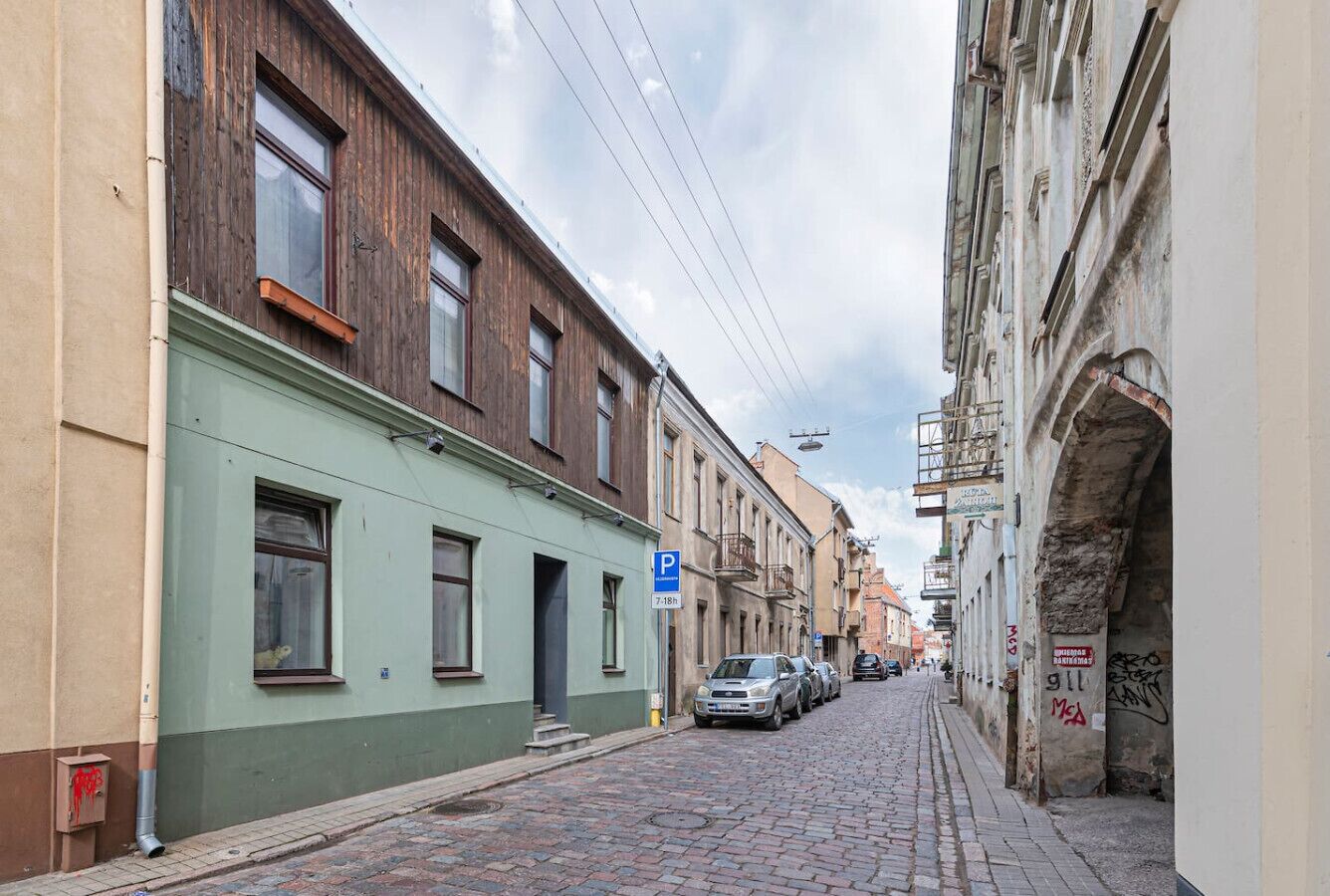 En smal brostensbelagt gade med historiske bygninger, et parkeringsskilt og en tydelig indgang.