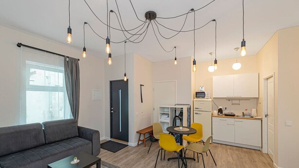 A modern apartment with a living area, a dining table with yellow chairs, a kitchenette, and a black door. - Downtown delight studio by Polo Apartments (Kaunas)
