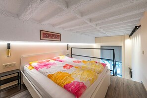 Ein Schlafzimmer mit Bett, Nachttisch, Wandlampe und einem Fenster mit Jalousien.