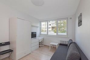 A compact room with a bed, a desk, a chair, a wardrobe, and a window with a view of buildings. - Pramonės ap 7 by Polo Apartments (Kaunas)