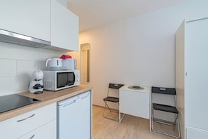 A compact kitchen with a microwave, coffee maker, and a small table with chairs. - Pramonės ap 7 by Polo Apartments (Kaunas)