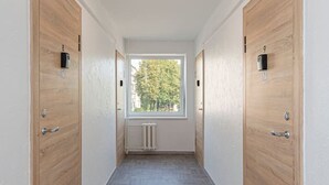 Un couloir avec deux portes en bois, un radiateur et une fenêtre donnant sur des arbres.