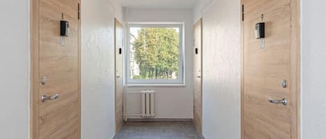 A corridor with two wooden doors, a radiator, and a window with a view of trees.