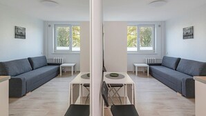 Ein modernes Wohnzimmer mit einer grauen Couch, einem kleinen weißen Tisch und einem Fenster mit Blick auf Bäume.