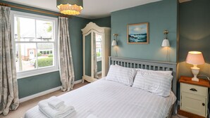 A bedroom with a bed, a nightstand, a mirror, and a window with curtains.
