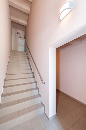 A staircase with a handrail, a light fixture on the wall, and a door at the top.