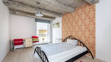 Een slaapkamer met een bed, een bureau, een stoel en een raam.