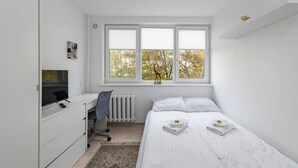 Une chambre à coucher comprenant un lit, un bureau, une chaise, un radiateur et une fenêtre avec des stores.