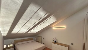 A bedroom with a sloped ceiling, a bed, a bedside table, a dresser, a radiator, and a wall-mounted light fixture. - Stefano's cozy apartment (Erba)