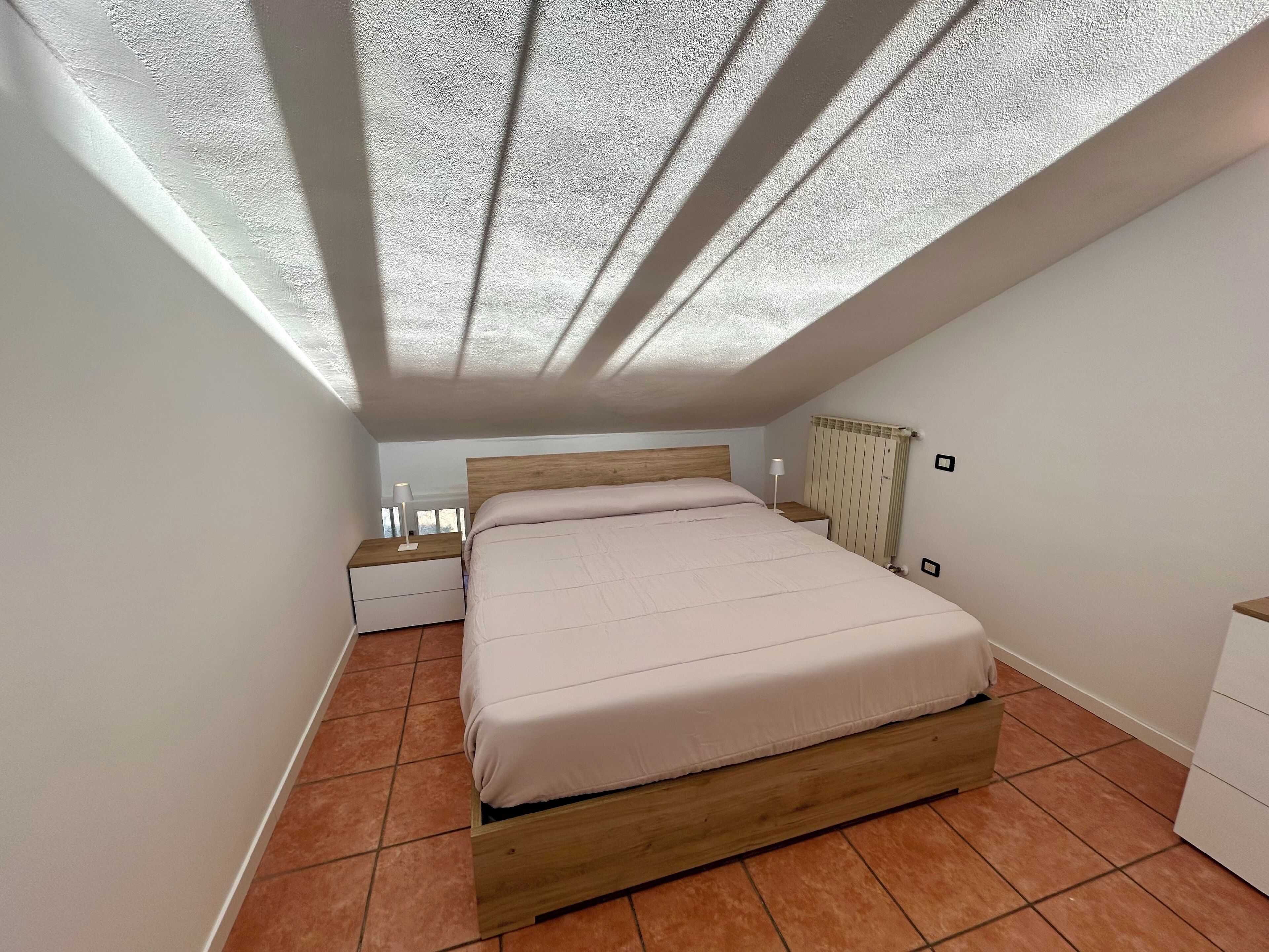 A bedroom with a wooden bed, a nightstand, a bedside table, and a radiator.