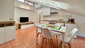 A compact kitchen with a dining area, a TV, and a small dining table with chairs. - Stefano's cozy apartment (Erba)