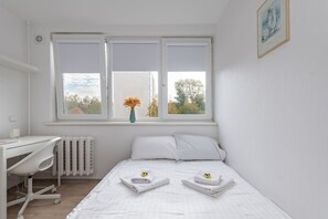 A bedroom with a bed, a desk, and a window with a view of trees.