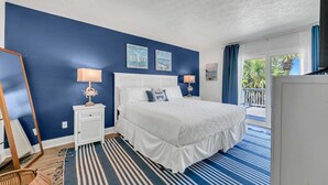 A bedroom with a large bed, a nightstand with lamps, a mirror, and a view of the outdoors through a sliding door. - Sandpiper Philosophy (Panama City Beach)