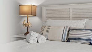 A neatly made bed with striped pillows, a lamp, and rolled towels on a white nightstand. - Sandpiper Philosophy (Panama City Beach)