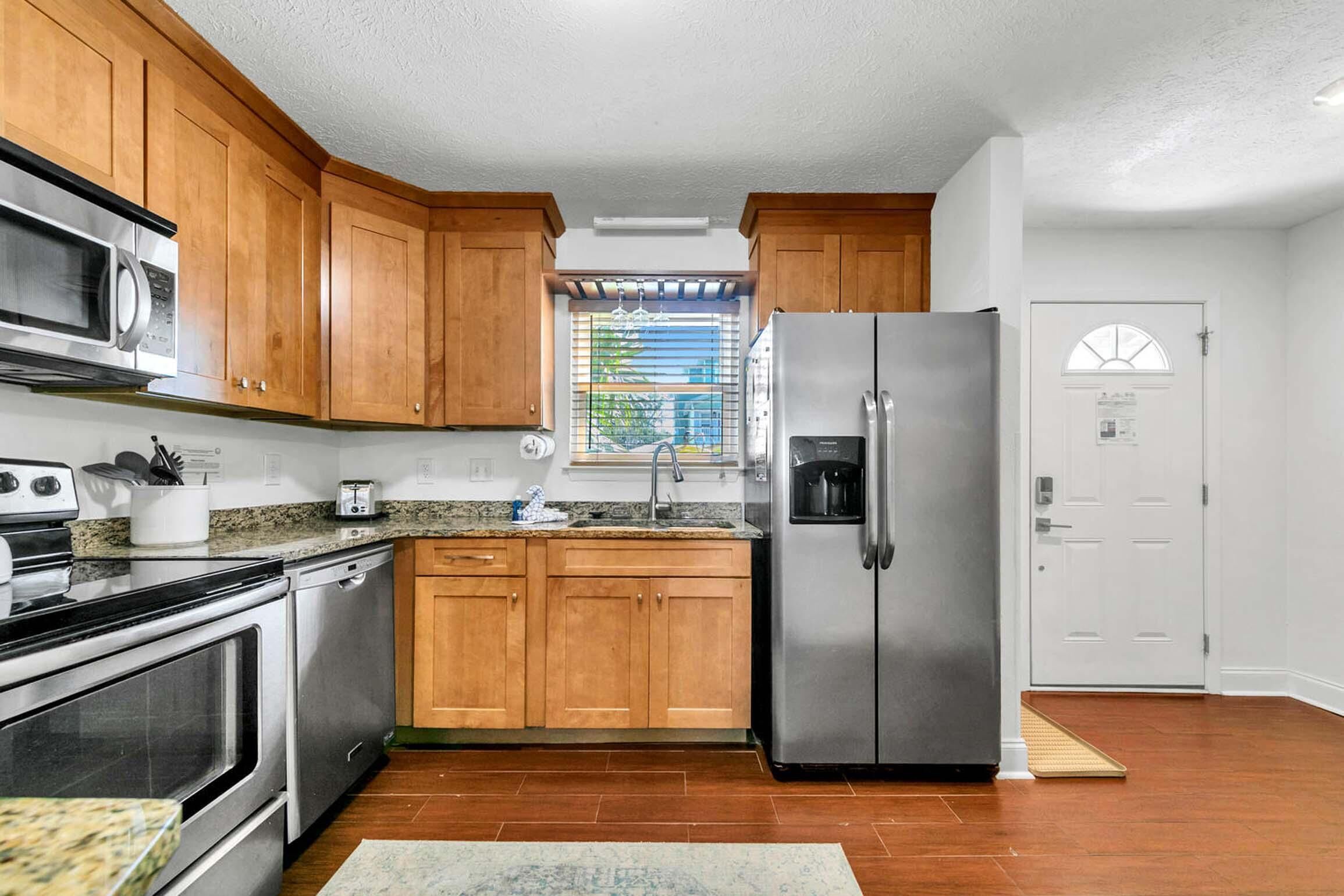 A kitchen with wooden cabinets, stainless steel appliances, a window with blinds, and a door with a window.