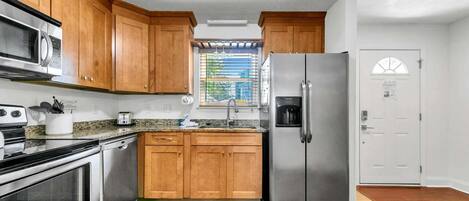 A kitchen with wooden cabinets, stainless steel appliances, a window with blinds, and a door with a window.