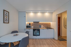 A modern kitchen with white cabinets, a dining table with chairs, and a small oven. - Luminious ap w balcony by PoloApartments (Kaunas)