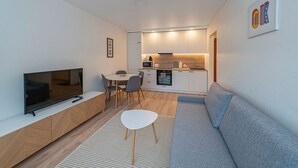 Ein kompakter Wohnbereich mit Flachbildfernseher, Esstisch mit Stühlen, einer Couch, einer Küchenzeile und einem kleinen Teppich.