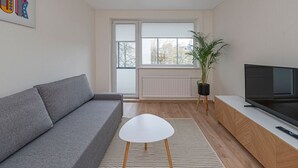Ein modernes Wohnzimmer mit grauem Sofa, einem weißen Couchtisch, einem Fernseher auf einem Holzboden und einer Topfpflanze.