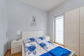 Un dormitorio con cama, mesitas de noche, lámpara, decoración en la pared y ventana con persianas.