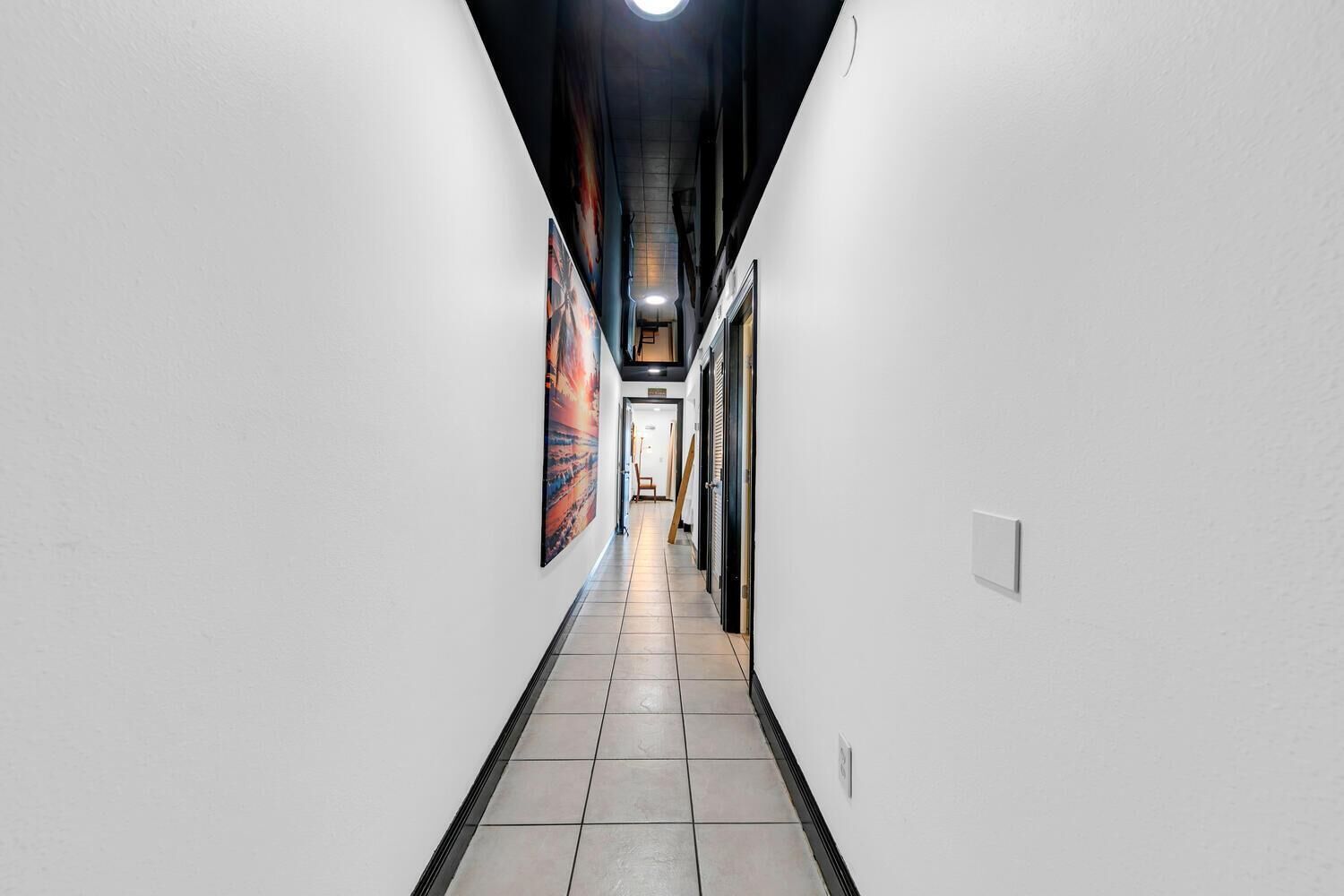 A narrow hallway with white walls, tiled floor, and a ceiling with exposed beams.