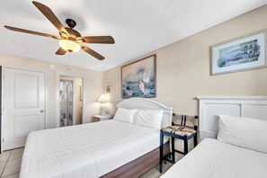 A hotel room with a large bed, a ceiling fan, a painting, and a view of the sea.