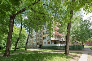 Un immeuble résidentiel à plusieurs étages, doté de balcons, entouré d’arbres et d’une clôture verte.
